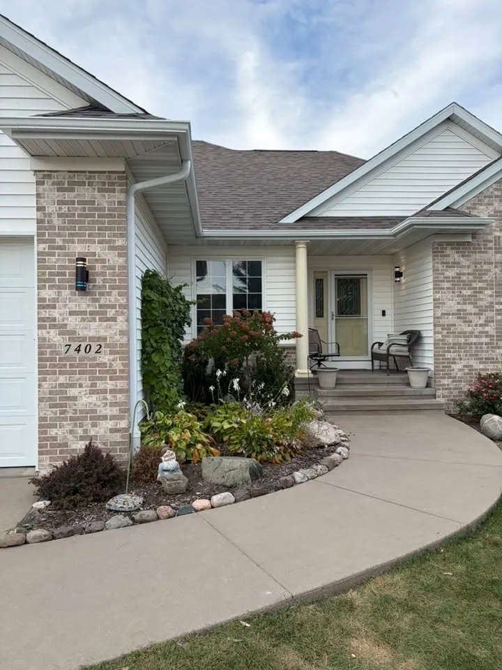 Brick and siding home with white gutters over a front porch and curved sidewalk
