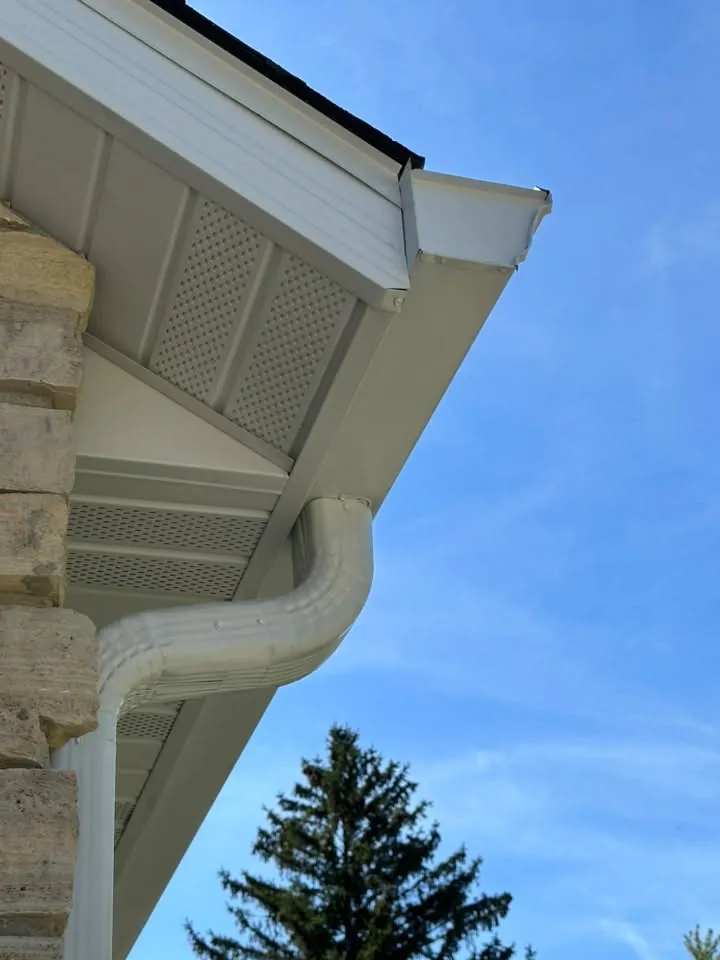 White downspout bent around a stone corner under a white fascia