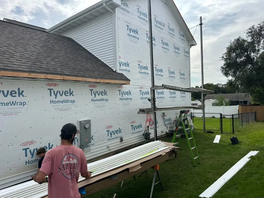 Crew member cutting siding beside a wall covered in house wrap during a siding install